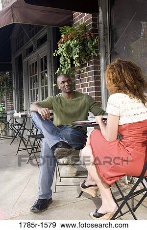 Stock Photo - Young couple sitting at a table at a sidewalk cafÄ. Fotosearch