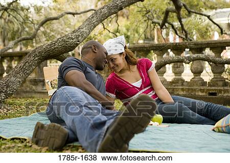 Stock Photo - Young couple sitting on a picnic blanket in a garden. Fotosearch