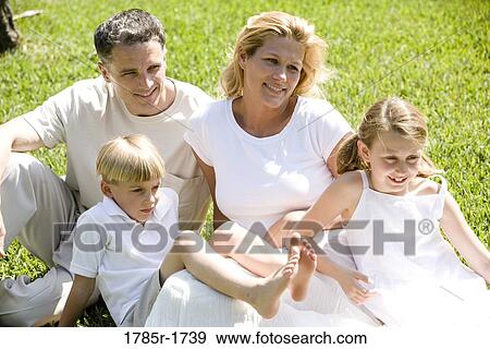 Stock Photo - Young family with young son and daughter sitting on grassy front lawn. Fotosearch