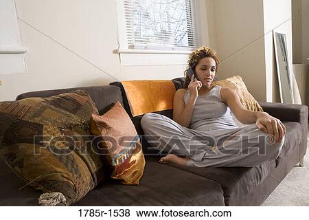Stock Photo - Young Hispanic woman relaxing on sofa talking on phone. Fotosearch