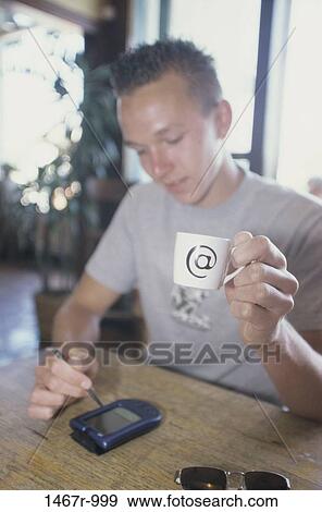 Young man holding a cup and writing on a hand held device View Large Photo Image Stock Photo - Young man holding a cup and writing on a hand held device. Fotosearch