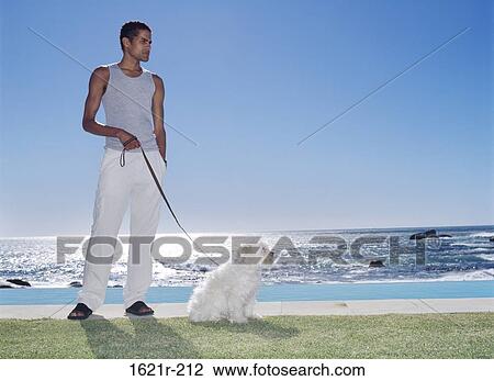 Stock Image - Young man holding a dog on a leash. Fotosearch
