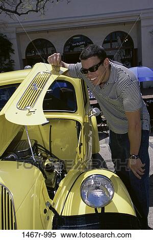Young man leaning against a vintage car smiling View Large Photo Image Stock Photography - Young man leaning against a vintage car smiling. Fotosearch