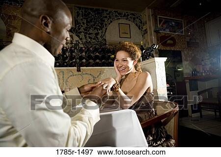 Young man putting engagement ring on woman's finger View Large Photo Image Stock Photo - Young man putting engagement ring on woman's finger. Fotosearch