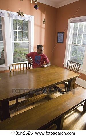 Young man sitting at table at home View Large Photo Image Stock Photography - Young man sitting at table at home. Fotosearch