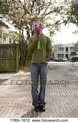 Young man standing on street covering his face with bouquet of flowers View Large Photo Image Stock Image - Young man standing on street covering his face with bouquet of flowers. Fotosearch