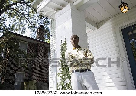 Stock Image - Young man standing outside a house. Fotosearch