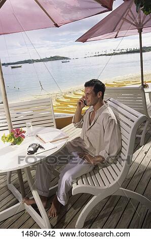 Stock Image - Young man talking on a mobile phone at the beach, Fiji. Fotosearch