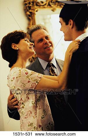 Stock Image - Young man wearing a graduation outfit with his parents standing in front of him. Fotosearch