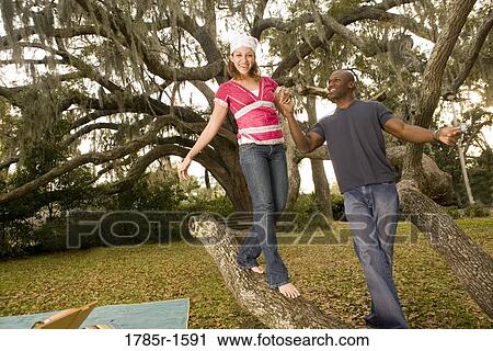 Stock Image - Young romantic couple balancing on oak tree branch. Fotosearch