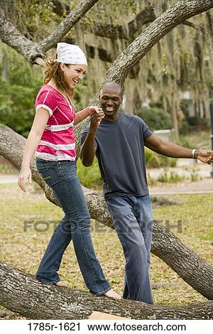 Stock Image - Young romantic couple balancing on oak tree branch. Fotosearch