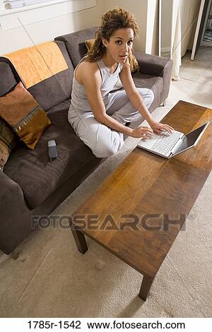 Stock Image - Young woman sitting on sofa using a laptop computer. Fotosearch