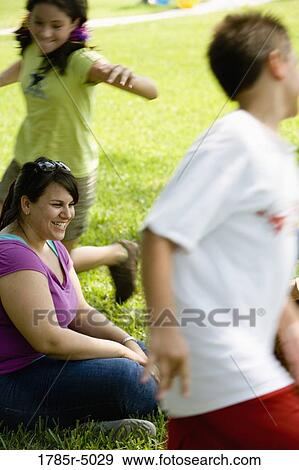 A boy and a girl running around their teacher sitting on the grass at a park View Large Photo Image Stock Photo - A boy and a girl running around their teacher sitting on the grass at a park. Fotosearch