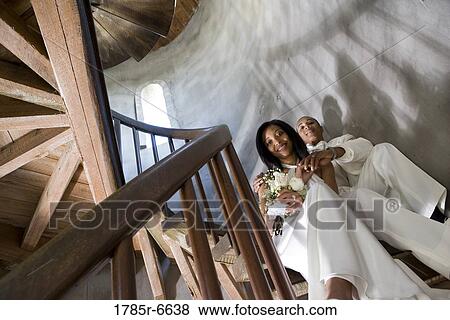 Stock Photo - A bride and groom in white sitting on a spiral staircase. Fotosearch
