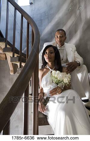 Stock Photograph - A bride and groom in white sitting on a spiral staircase. Fotosearch