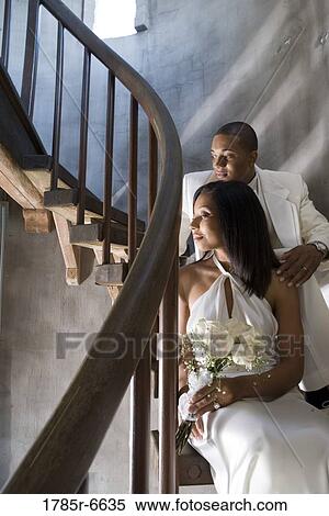 Stock Photography - A bride and groom in white sitting on a spiral staircase. Fotosearch