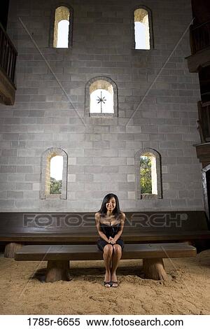 Stock Photography - A bride in a black dress sitting on a bench inside a medieval castle. Fotosearch