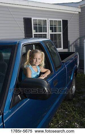 Stock Photography - A girl playing in parked old truck in front of trailer home. Fotosearch