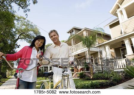 Stock Image - A mature couple walking with bicycles in neighborhood of two-storey houses. Fotosearch