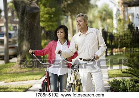 A mature inter-racial couple walking with bicycles in their neighborhood View Large Photo Image Stock Image - A mature inter-racial couple walking with bicycles in their neighborhood. Fotosearch