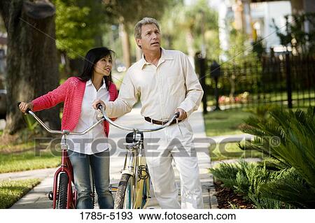 A mature inter-racial couple walking with bicycles in their neighborhood View Large Photo Image Stock Image - A mature inter-racial couple walking with bicycles in their neighborhood. Fotosearch