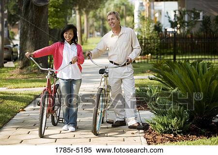 A mature inter-racial couple walking with bicycles in their neighborhood View Large Photo Image Stock Photography - A mature inter-racial couple walking with bicycles in their neighborhood. Fotosearch