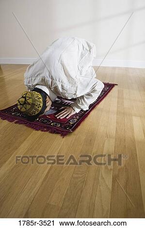 Stock Image - A Muslim man bowing head on a prayer mat. Fotosearch