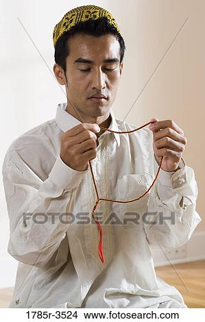 Picture - A Muslim man praying with prayer beads. Fotosearch