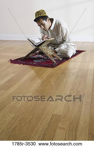 Stock Image - A Muslim man reading Koran on a prayer mat. Fotosearch