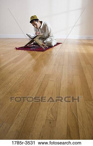 Stock Image - A Muslim man reading Koran on a prayer mat. Fotosearch