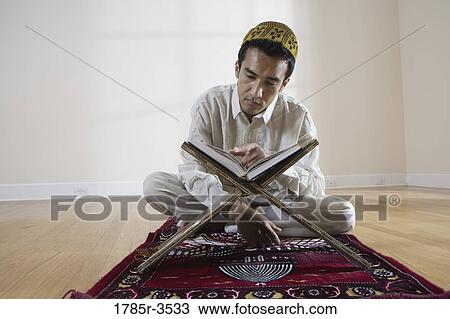 Stock Image - A Muslim man reading Koran on a prayer mat. Fotosearch