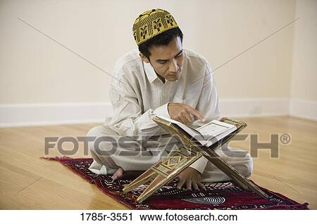Stock Image - A Muslim man reading Koran on a prayer mat. Fotosearch