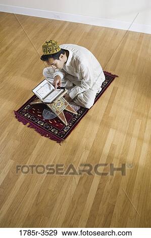 Stock Photo - A Muslim man reading Koran on a prayer mat. Fotosearch