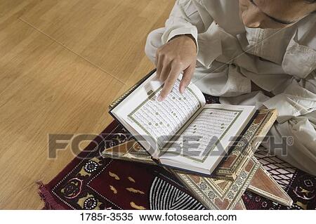 Stock Photography - A Muslim man reading Koran on a prayer mat. Fotosearch