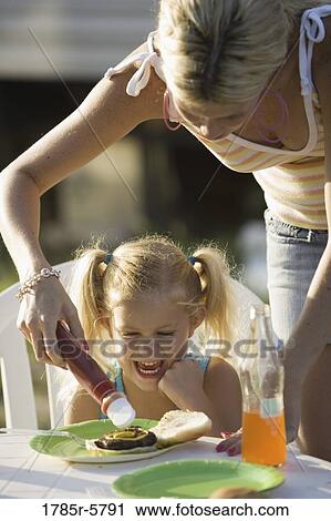 A woman putting ketchup on a young girl's burger View Large Photo Image Stock Image - A woman putting ketchup on a young girl's burger. Fotosearch