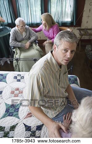 Stock Image - Adult children visiting and comforting senior parents in bedroom. Fotosearch