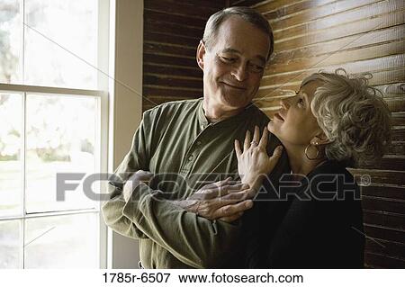 Affectionate mature couple in darkened room next to window frame View Large Photo Image Stock Photo - Affectionate mature couple in darkened room next to window frame. Fotosearch