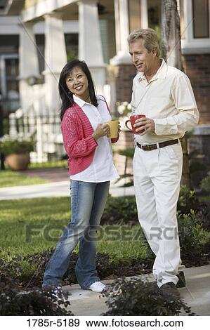 Affectionate mature inter-racial couple holding coffee mugs in front of their house View Large Photo Image Stock Photo - Affectionate mature inter-racial couple holding coffee mugs in front of their house. Fotosearch