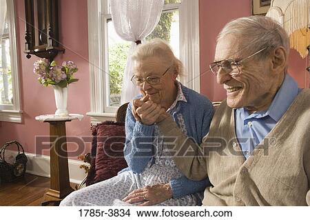 Affectionate senior couple sitting on sofa in living room View Large Photo Image Picture - Affectionate senior couple sitting on sofa in living room. Fotosearch