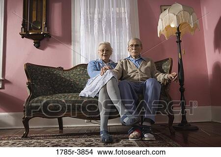 Affectionate senior couple sitting on sofa in living room View Large Photo Image Picture - Affectionate senior couple sitting on sofa in living room. Fotosearch