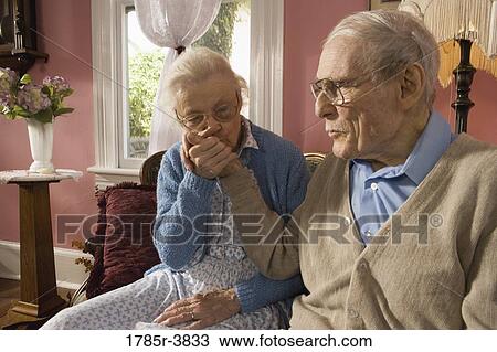 Stock Image - Affectionate senior couple sitting on sofa in living room. Fotosearch