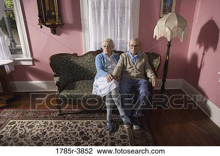 Affectionate senior couple sitting on sofa in living room View Large Photo Image Stock Image - Affectionate senior couple sitting on sofa in living room. Fotosearch