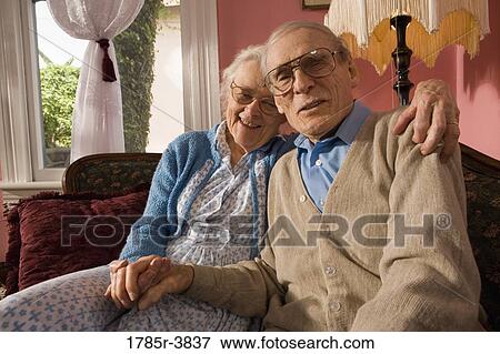 Stock Photo - Affectionate senior couple sitting on sofa in living room. Fotosearch