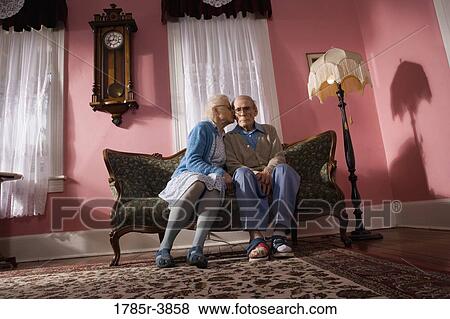 Stock Photo - Affectionate senior couple sitting on sofa in living room. Fotosearch