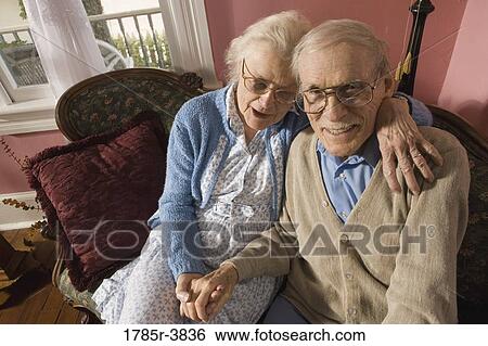 Stock Photograph - Affectionate senior couple sitting on sofa in living room. Fotosearch