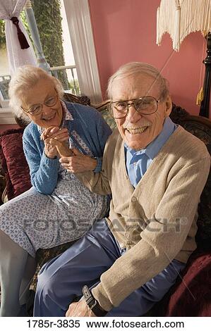 Affectionate senior couple sitting on sofa in living room View Large Photo Image Stock Photography - Affectionate senior couple sitting on sofa in living room. Fotosearch