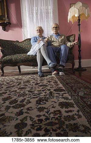 Affectionate senior couple sitting on sofa in living room View Large Photo Image Stock Photography - Affectionate senior couple sitting on sofa in living room. Fotosearch