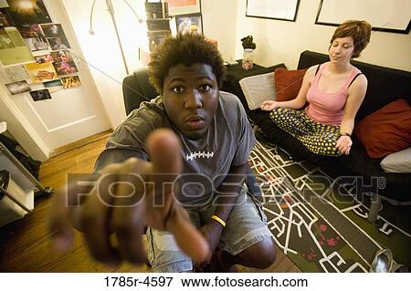 African man sitting in living room while woman meditates in background View Large Photo Image Stock Photo - African man sitting in living room while woman meditates in background. Fotosearch