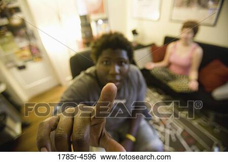 African man sitting in living room while woman meditates in background View Large Photo Image Stock Photograph - African man sitting in living room while woman meditates in background. Fotosearch