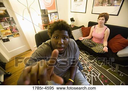 Stock Photography - African man sitting in living room while woman meditates in background. Fotosearch